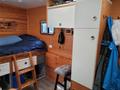 Interior of a 2022 Royal Camper featuring a bed with blue bedding a white cabinet a wooden ladder and a gray stool