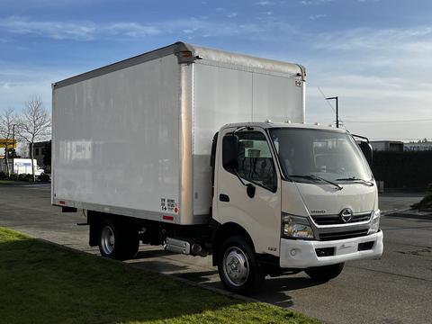 A 2015 Hino 195 box truck with a white cargo area and a light-colored cab parked on a street