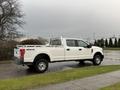 A white 2017 Ford F-350 SD pickup truck with a utility bed and ladder racks parked on a wet surface