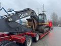 A 2014 John Deere 350G excavator mounted on a flatbed trailer with tracks and a large arm