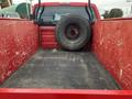 A red truck bed of a 2011 Ford F-250 SD with a spare tire resting against the back wall and a textured rubber mat on the floor