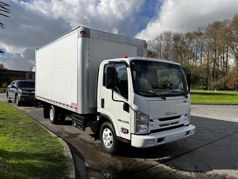 A white 2016 Isuzu NPR box truck with a large cargo area and dual rear wheels parked on a driveway