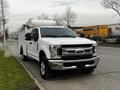 A 2019 Ford F-350 Super Duty truck in white with a utility body and chrome grille parked on the street