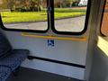 Interior view of a bus with blue patterned seats and a yellow grab bar installed next to a sign indicating wheelchair accessibility