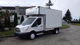 A white 2018 Ford Transit box truck with a tall cargo area and a flatbed design parked on a street