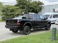 A black 2024 RAM 2500 pickup truck with a crew cab and off-road tires is parked, showcasing its robust design and prominent RAM branding on the tailgate