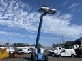 A blue 1997 Genie S-65 4X4 lift with a raised work platform and large wheels