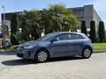 A blue 2018 Kia Rio5 hatchback parked on a pavement with palm plants in the background