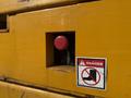 A close-up view of a yellow Haulotte Compact machine featuring a red button and a warning sticker indicating danger with a crossed-out boot symbol
