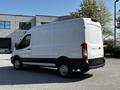 A white 2021 Ford Transit van with a high roof and sliding side door parked on a gravel surface