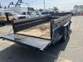 A black dump trailer with an open bed containing dirt, featuring a dual-axle setup and a chain securing the tailgate