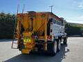 A yellow and silver 2005 Volvo VND 122 dump truck with a sign reading KEEP BACK 15 m on the rear and a ladder on the side for access