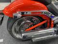 Close-up of a 2024 Harley Davidson Fat Boy showing the rear wheel, chrome exhaust pipes, and orange frame accents