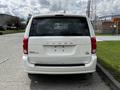 A white 2011 Dodge Grand Caravan viewed from the rear with no license plate installed and the Dodge logo visible on the back door