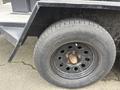 A close-up of a tire mounted on a black metal trailer rim showing visible wear and rust along the rim and bolt area