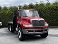 A red 2011 International 4400 flatbed truck with a black bed and chrome accents parked in a lot