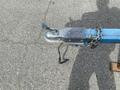 A close-up view of a metal hitch on a blue trailer with a chain securing it, featuring a latch and a hook for attaching to a vehicle