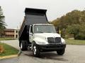 A 2006 International 4200 dump truck with a white cab and black dump bed parked on a paved surface