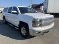A white 2015 Chevrolet Silverado 1500 with chrome accents and a truck bed cover parked at an angle showing its front and side view