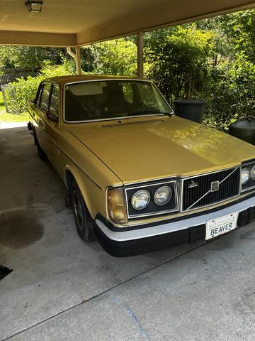 A 1978 Volvo 244 in yellow with a black grille and headlights parked under a shelter showcasing its classic sedan design and vintage appeal