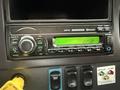 The image shows a Freightliner truck's audio system featuring a digital display with time settings buttons for band tuning and phone connectivity along with various control buttons