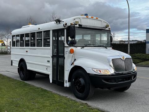 A white 2013 International 4200 school bus with black wheels and a front door, featuring large windows on the sides and a prominent grille