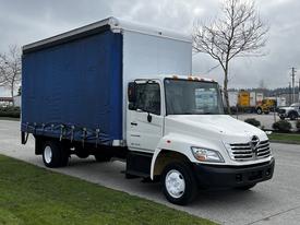 A white 2006 Hino 268 truck with a blue cargo box and a flatbed design parked on the side of the road
