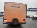 A 2015 Winnebago Of Indiana Travel Trailer featuring an orange rear with the brand name Winnebago displayed prominently on the back and a spare tire mounted beneath the rear bumper