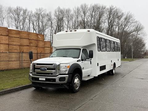 A white 2011 Ford F-550 bus with large windows parked on a wet surface