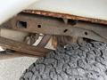 Close-up of a 2010 Ford F-150's undercarriage showing a rusty metal frame and a textured rubber tire tread