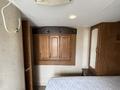 A wooden cabinet with three doors mounted on a wall inside a trailer with a mattress visible below it