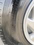 Close-up of a winter tire with the text "Winter Studless" visible on the sidewall and silver alloy wheel rim in the foreground