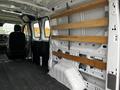 A 2023 Ford Transit interior featuring a spacious cargo area with wooden shelving mounted on the walls and a driver's seat visible in the front