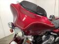 A close-up of a red 2005 Harley-Davidson FLHTCI motorcycle featuring a large windshield and chrome accents on the handlebars and front lights