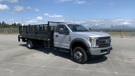 A 2019 Ford F-550 truck with a metallic silver body and a black flatbed secured with a metal mesh railing