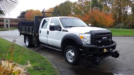 A white 2011 Ford F-550 with a flatbed and black stake sides parked on a driveway