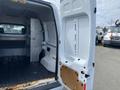 A 2013 Ford Transit Connect van with its rear doors open revealing a spacious cargo area with metal shelving and a wooden panel on the floor