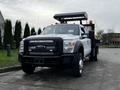 A white 2015 Ford F-550 truck with a flatbed and equipment rack featuring orange warning lights and a black grille with a logo on the front