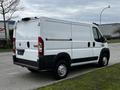 A white 2018 RAM Promaster van parked on the street with a simple and utilitarian design featuring a tall cargo area and rear doors that swing open