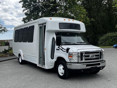 A 2013 Ford Econoline shuttle bus with a white exterior and large windows parked with its sliding door open