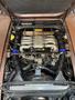 Engine compartment of a 1983 Porsche 928 showcasing the V8 engine with multiple pipes and hoses prominently positioned
