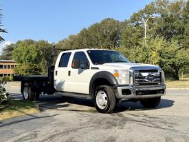A white 2014 Ford F-550 truck with a flatbed, featuring a spacious cabin and dual rear wheels, parked on a pavement with clear visibility of its front and side angles