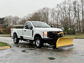 A 2023 Ford F-250 pickup truck equipped with a yellow snow plow attached to the front and facing forward