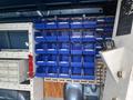 A 2010 Ford Econoline van interior displaying a wall-mounted storage system with numerous blue bins organized in rows