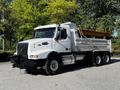 A white 2005 Volvo VND 122 dump truck with a yellow bed and black front grille parked on a road with trees in the background