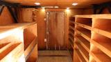 Interior of a storage vehicle featuring wooden shelves along the walls and a door at the back with a metal lock