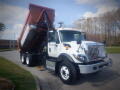 A white 2016 International WorkStar 7500 dump truck with an orange dump bed raised and six wheels visible