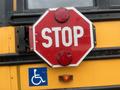 A red octagonal stop sign with white letters prominently displayed on the side of a yellow school bus