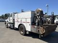A 2007 International 7300 truck with a white and gray body featuring a utility bed equipped with various compartments and a reel assembly at the rear
