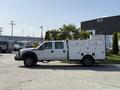 A white 2015 Ford F-550 truck with a utility bed featuring multiple compartments and a ladder rack on top